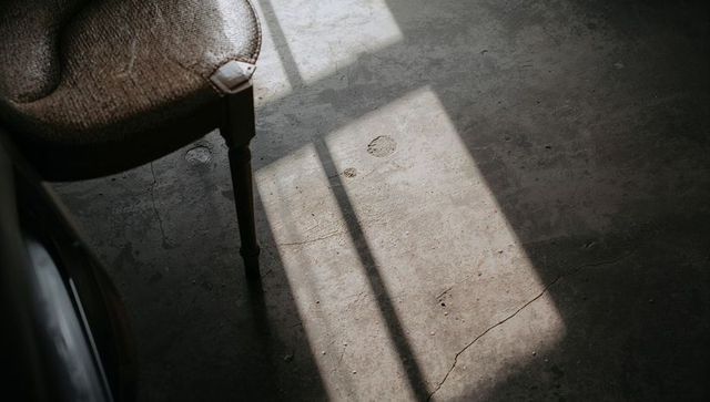 Sunlit Concrete Floor with Window Grid Shadows, Cracks and Vintage Wooden Chair Leg