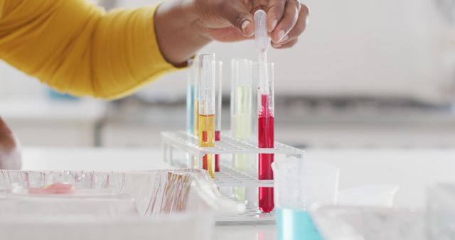 This stock photo shows a scientist conducting an experiment by adding substances into test tubes containing colored solutions. Ideal for use in educational materials, science-related articles, laboratory safety guides, or promotional content for scientific research and development.