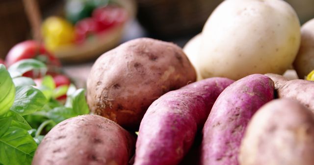 Assorted fresh potatoes displayed with other vegetables in the background. Featured prominently are regular potatoes and red-skinned sweet potatoes. Ideal for use in food-related content, healthy eating promotions, grocery store advertisements, recipes, and farm-to-table concepts.