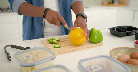 Man slicing yellow bell pepper and cucumber while preparing healthy meal prep containers