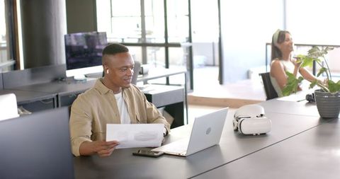 Smiling Businessman Reviewing Documents with Technology in Modern Office