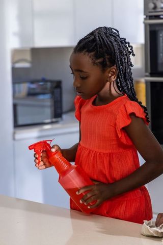 African american girl inspecting red spray bottle on modern kitchen counter in red dress