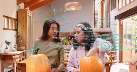 Women carving pumpkins with augmented reality interface in cozy rustic kitchen