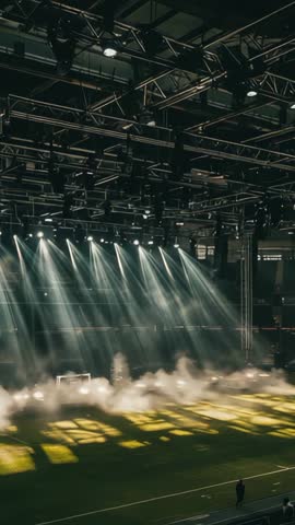 Vertical video of fog-filled stadium under dramatic spotlights with worker walking sideline