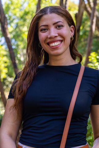 Smiling african american woman standing in sunlit park wearing black top and crossbody
