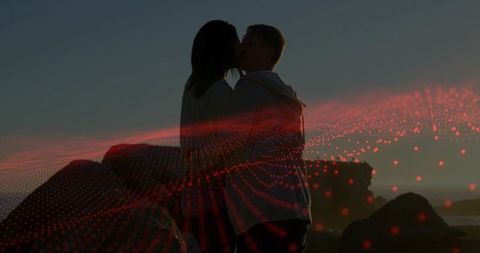 Kissing couple silhouette on rocky shore at sunset with red digital particle overlay