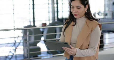 Young professional woman using tablet in modern office lobby with mezzanine and railing