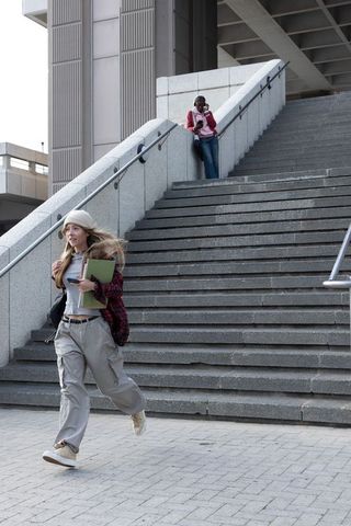 Diverse students running across urban campus stairs with notebooks and smartphone