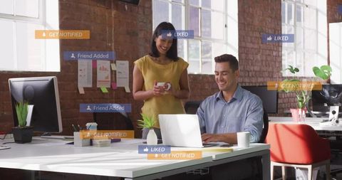 Colleagues collaborating on laptop in bright open-plan office with social media notifications