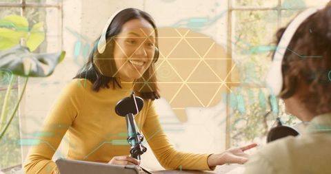 Sunlit podcast duo recording with headphones and microphones in bright creative workspace