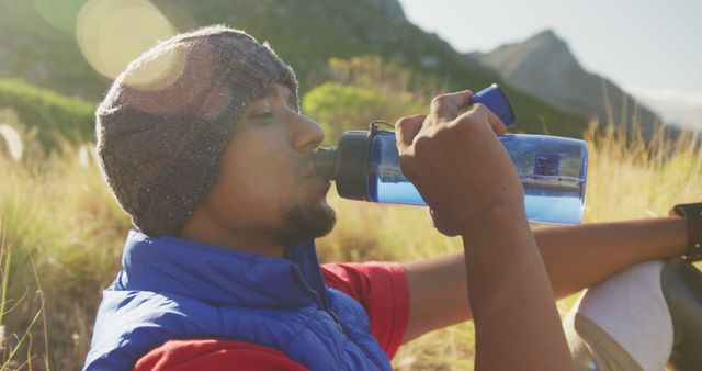 Close up of fit, disabled biracial man with prosthetic leg, enjoying his time on a trip to the mountains, hiking, sitting on the dirt road, taking a break, drinking water, on a sunny day