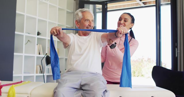 Senior man exercising with a resistance band under the guidance of a female physiotherapist. Ideal for depicting physical rehabilitation, elder health, exercise routines, fitness programs, medical support. Suitable for healthcare promotion, elderly fitness programs, physiotherapy advertisements.