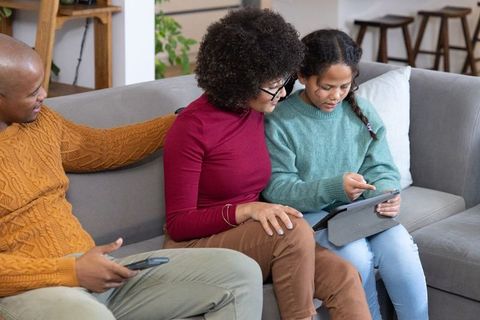 Multigenerational diverse family sitting on couch using tablet and remote for bonding
