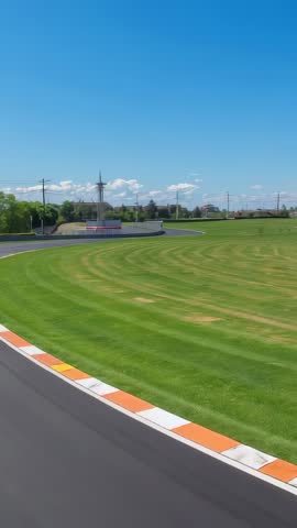 Vertical track camera tracing left-hand bend on racing circuit with orange curbstones