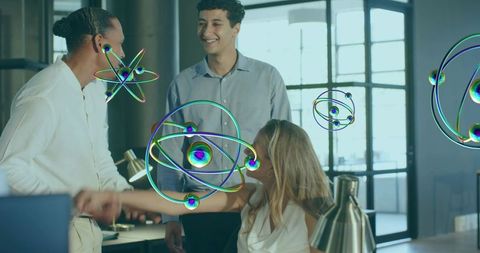 Colleagues shaking hands in office with holographic atom graphics for teamwork and innovation