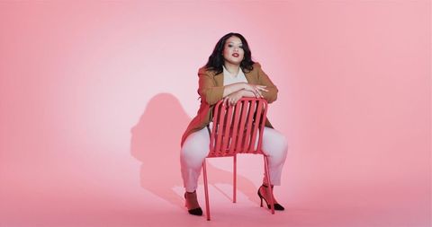 Confident plus size woman sitting on red chair in minimalist pink studio
