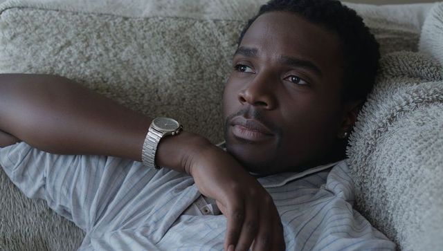 Reclining man on sofa gazing thoughtfully wearing silver watch and striped shirt