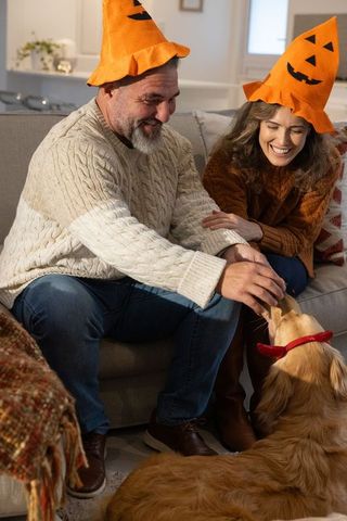 Couple wearing pumpkin hats feeding golden retriever on cozy autumn evening