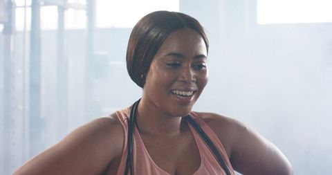 African american woman in pink tank smiling holding jump rope after gym workout