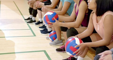 Female volleyball players sitting on bench holding balls showing teamwork and focus