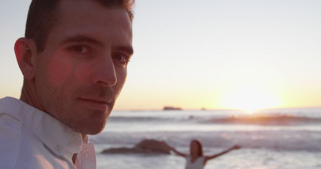 Man enjoying beach at sunset with woman in background - Download Free Stock Images Pikwizard.com