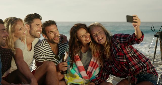 Group of friends gathered on a beach at sunset, capturing the moment with a selfie. Great for promoting summer vacations, beach parties, outdoor gatherings, social media, celebration events, and lifestyle blogs emphasizing friendship and leisure.