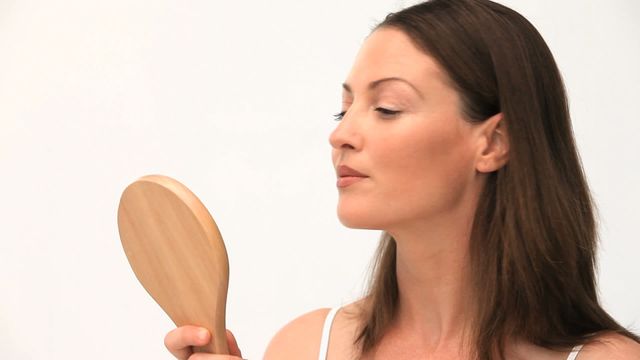 A woman attentively plucking her eyebrows while holding a small hand mirror. This video is ideal for content related to beauty routines, personal grooming, self-care products, beauty tutorials, and health and wellness articles.