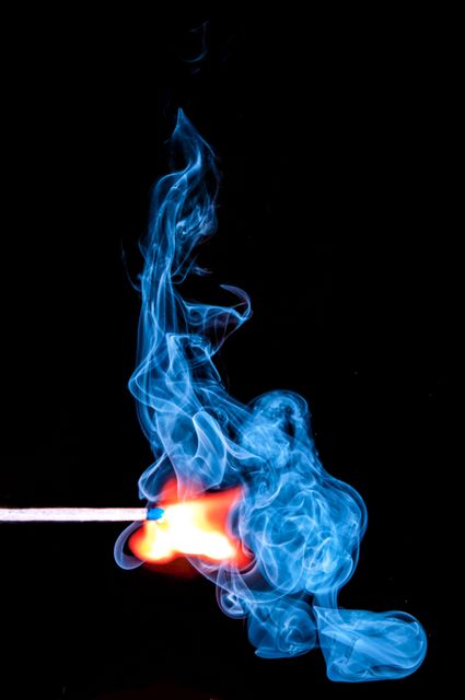 Dynamic close-up of a matchstick igniting, producing a striking blue smoke and orange flame. Use for chemistry and physics lessons, fire safety demonstrations, or artwork focused on fire elements.