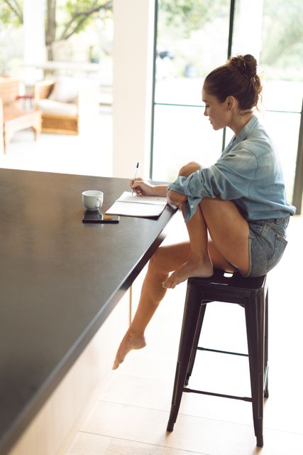 Side view of woman writing on notepad on worktop in kitchen at comfortable home