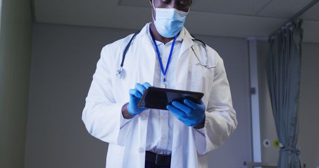 Healthcare professional wearing mask and gloves using tablet in hospital. Can be used to represent modern medical practices, medical technology integration, professionalism in healthcare, patient data security, and efficient patient management.