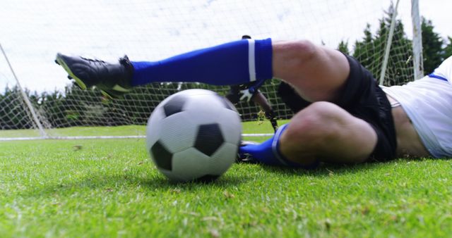 Soccer player is executing a sliding tackle near their goal on a grassy field. This dynamic and action-packed image is perfect for illustrating moments of competitive sports, the urgency of defending the goal, or as a representation of teamwork and athleticism in soccer-related editorial content, advertisements, or promotional materials.