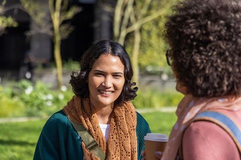Multicultural female students sharing coffee and chatting on sunny campus green space