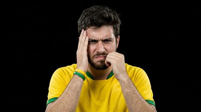 Young man holding temple and grimacing in yellow sports shirt showing stress and concentration