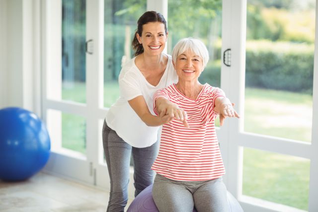 Female coach assisting senior woman with home exercise, promoting healthy lifestyle and active aging. Ideal for use in articles about fitness, personal training, senior health, wellness programs, and physical therapy. Can be used in advertisements for fitness equipment, personal training services, and health care facilities.