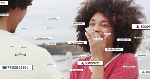 Laughing woman covering mouth on waterfront with floating social media labels, notifications
