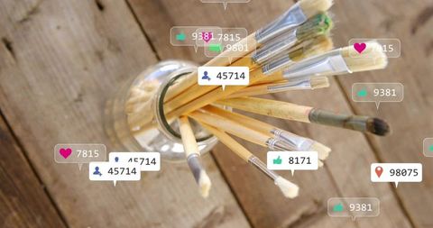 Overhead paintbrushes sitting in glass jar with social media notification badges on rustic wood