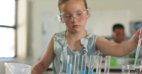 Young girl conducting science experiment with pipette and test tubes in school lab