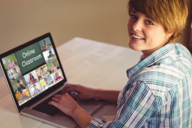 A young student engaged in an online classroom session via video conference. The student is smiling while using a laptop, attendng a virtual learning environment. This image can be used for educational websites, e-learning platforms, online tutoring services, or articles on remote education and virtual classrooms.