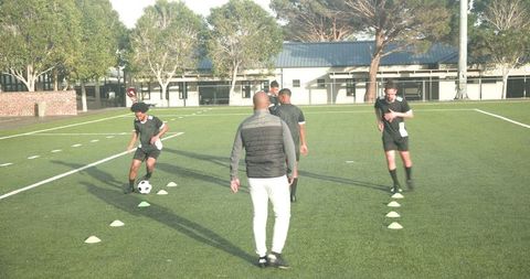 Coach guiding soccer players in dribbling drills on school field