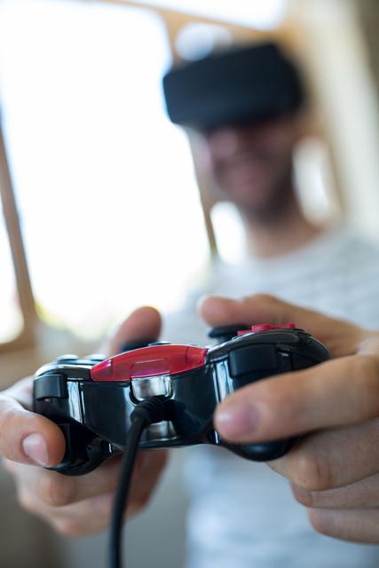 Man wearing virtual reality headset and holding a game controller, engaging in an immersive gaming experience. Ideal for use in articles or advertisements related to gaming technology, virtual reality, entertainment, and modern digital innovations.