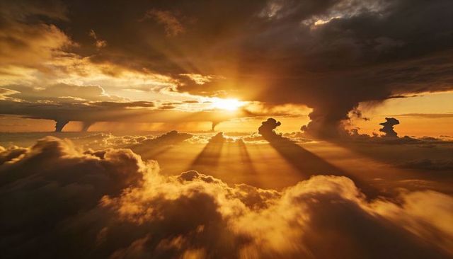 Golden sunset above cloudscape casting dramatic sunbeams through towering cumulus storm columns