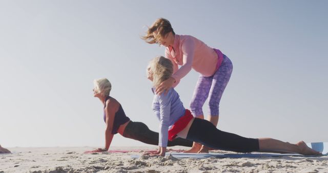 Diverse women with female yoga instructor wearing sports clothes doing yoga and stretching at beach. Sport, friendship, healthy and active lifestyle.
