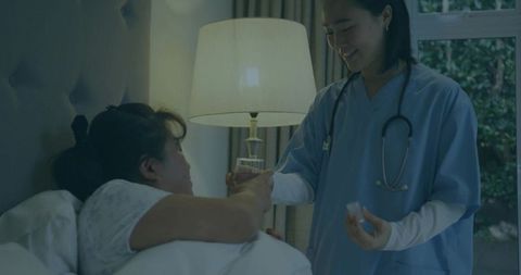 Nurse administering medication and glass of water at bedside during home care visit