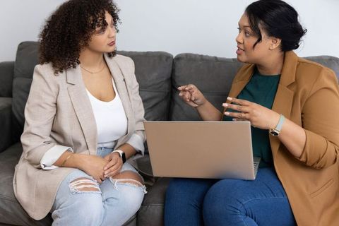 Two women collaborating on laptop during casual office consultation and mentoring on couch