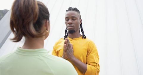 Diverse pair meditating outdoors, black man praying hands together practicing mindfulness