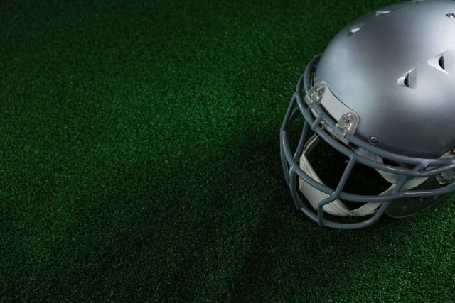 This image shows a close-up of an American football helmet lying on green artificial turf. It can be used for sports-related articles, advertisements for football gear, safety equipment promotions, or as a visual for athletic events and competitions.