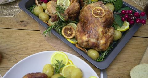 Rustic roasted chicken resting with lemon, rosemary and baby potatoes on tray for festive dinner