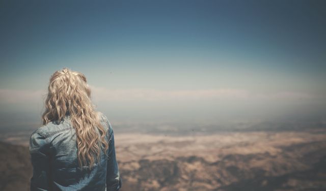 Blonde woman with long wavy hair, wearing denim jacket, standing and appreciating vast mountain landscape. Perfect for travel inspiration, serene natural environments, and exploring the great outdoors. Ideal for blogs, travel agencies, environmental conservation, and wellness content.