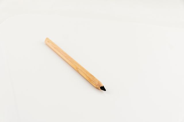This image features a single wooden pencil lying on a white background, presenting a clean and minimalistic look. Ideal for use in articles and advertisements related to stationary, education, office supplies, or minimalist design concepts.