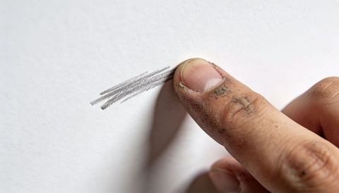 Smudging graphite with dirty fingertip creating subtle shading on white paper